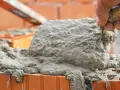 Ręka murarza nakłada świeżą zaprawę na cegły.