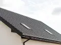 Nowy dach z dachówki w kolorze RAL 9011, z oknem dachowym i białym tynkiem.