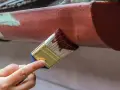 Ręka maluje pędzlem rynienkę aluminiową na brązowo. Odpowiedź na pytanie: czym pomalować aluminium.