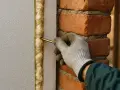 Ręka w rękawicy aplikuje piankę montażową, uszczelniając szczelinę między styropianem a ceglanym murem.
