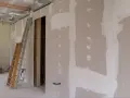 Scianka dzialowa z plyty kartonowo gipsowej w trakcie prac. Widoczne drabiny, instalacje i otwór drzwiowy.