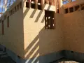 Budowa domu, ściany zewnętrzne z płyt OSB, widoczne okna i fundament.