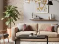 Przytulny salon z kanapą w kolorze słomkowym, szarymi fotelami, ceglaną ścianą i dużą rośliną.
