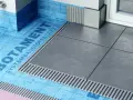 Systemowa hydroizolacja łazienki z niebieską membraną Botament i szarymi płytkami.
