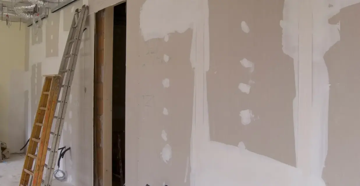 Scianka dzialowa z plyty kartonowo gipsowej w trakcie prac. Widoczne drabiny, instalacje i otwór drzwiowy.