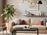 Przytulny salon z kanapą w kolorze słomkowym, szarymi fotelami, ceglaną ścianą i dużą rośliną.