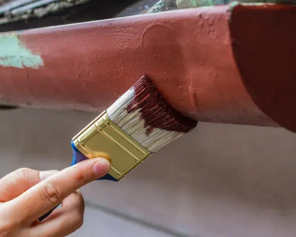 Ręka maluje pędzlem rynienkę aluminiową na brązowo. Odpowiedź na pytanie: czym pomalować aluminium.