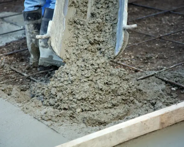 Wylewanie świeżego betonu na zbrojenie. Trwa naprawa betonu, widać buty pracownika i metalowe pręty.