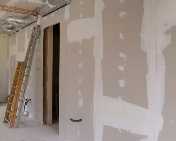 Scianka dzialowa z plyty kartonowo gipsowej w trakcie prac. Widoczne drabiny, instalacje i otwór drzwiowy.