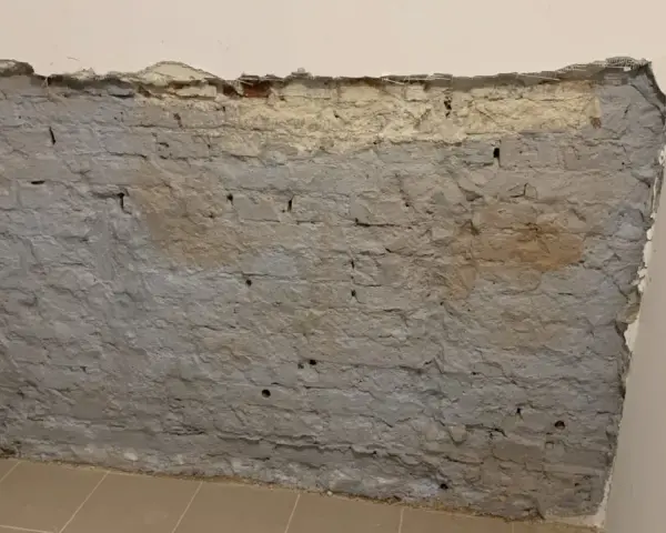 Fragment odsłoniętej, starej ceglanej ściany z szarym tynkiem i fragmentami żółtego podkładu.
