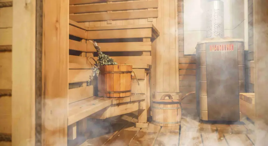 Drewniana sauna z piecem, ławami i wiaderkiem z miotełką. Idealne miejsce, by dowiedzieć się, jak zbudować saunę i odpocząć.