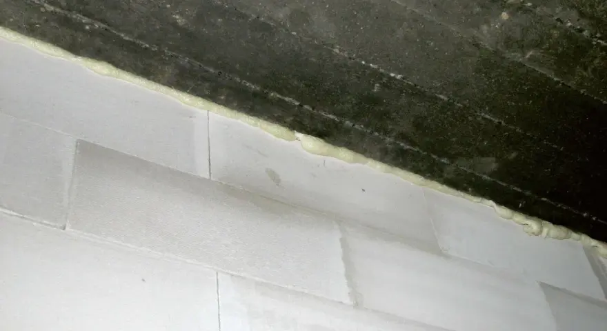 Piana montażowa wypełnia szczelinę między betonowym stropem a białą ścianą z bloczków, tworząc dylatację.