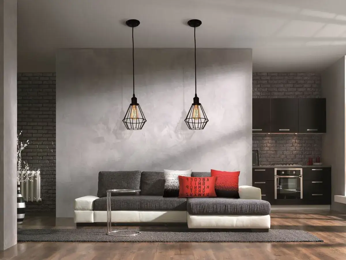Nowoczesny salon z szarą sofą i kuchnią w tle, oddzielony od salonu betonową ścianą działową.